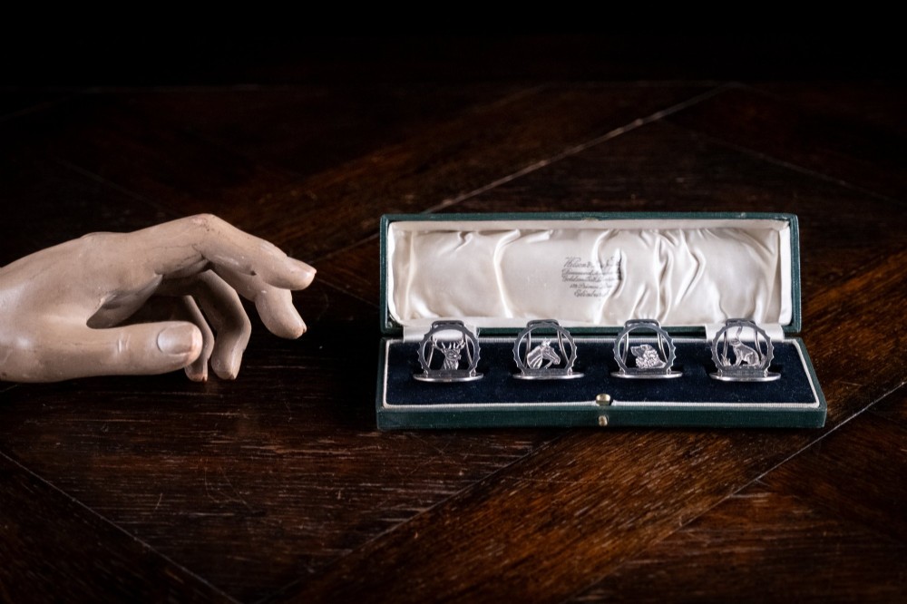 A set of four sterling silver animal-themed menu holders featuring a stag, horse, dog, and hare, presented inside a fitted green display box. View IX