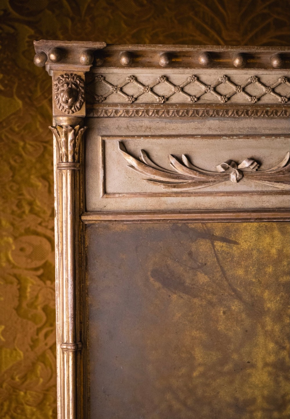 A large Regency style painted and gilded pier mirror featuring classical fluted columns, lion mask corner accents, a ball-ornament cornice, and distressed mirror glass. View IX