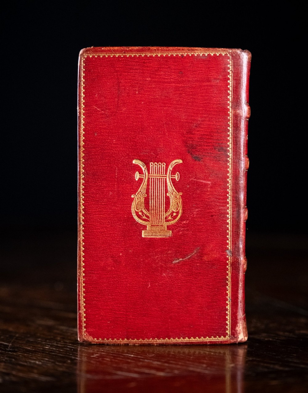 An 1821 miniature book bound in red leather featuring gilt spine tooling, raised bands, and gold lettering. View IV