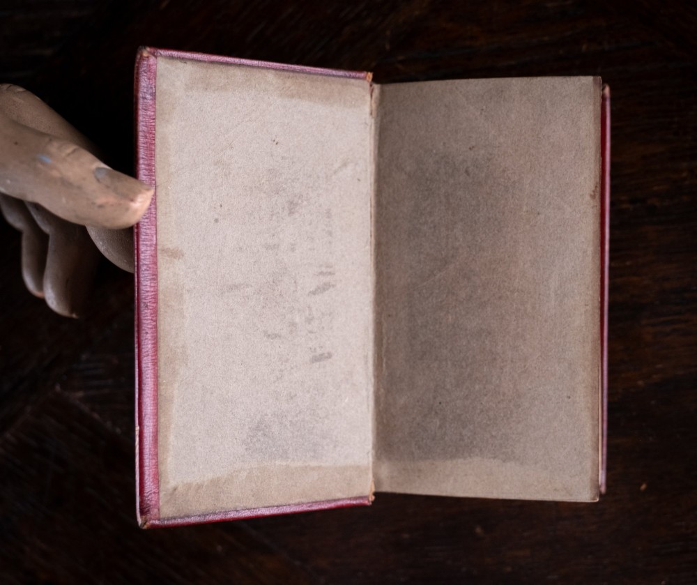 An 1821 miniature book bound in red leather featuring gilt spine tooling, raised bands, and gold lettering. View VI