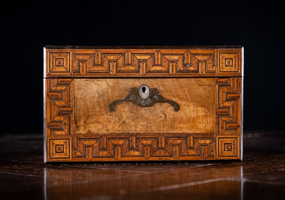 A rectangular Victorian walnut tea caddy featuring geometric parquetry borders along the edges and a brass and mother of pearl inlaid escutcheon on the front face. View IV