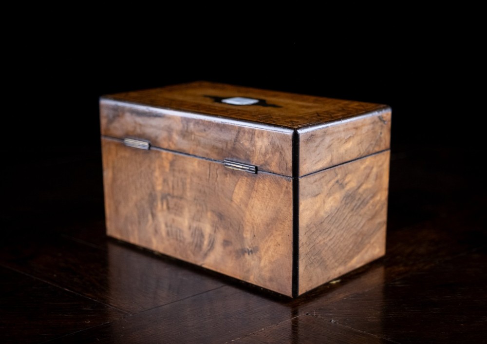 A rectangular Victorian walnut tea caddy featuring geometric parquetry borders along the edges and a brass and mother of pearl inlaid escutcheon on the front face. View XI