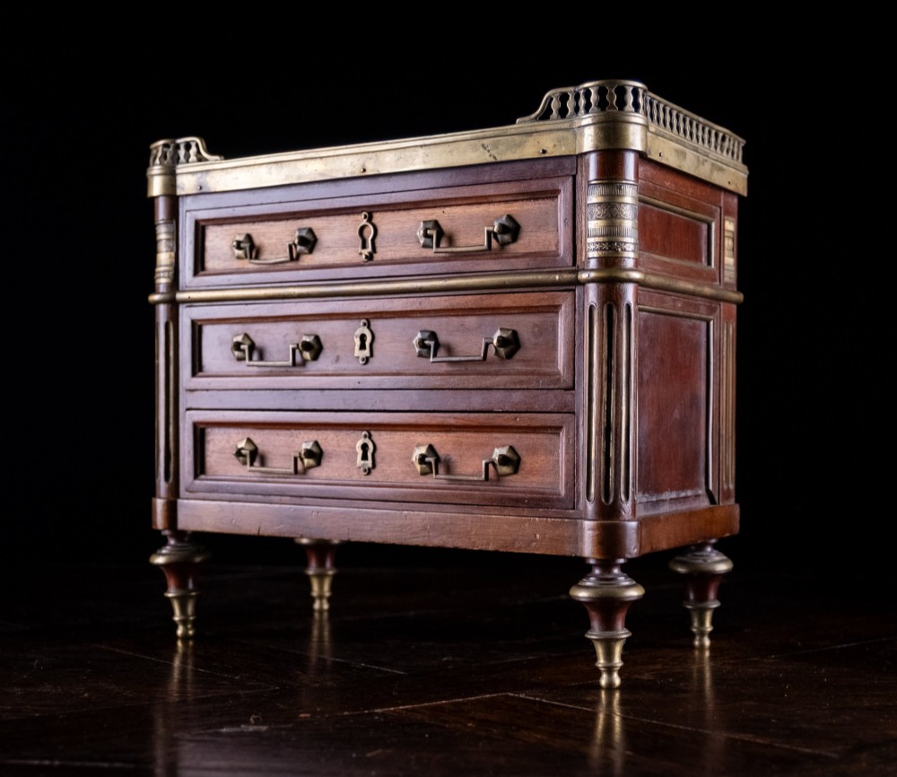 A miniature Louis XVI style mahogany chest of three drawers featuring a white marble top, pierced brass gallery, and metal drawer handles. View IV
