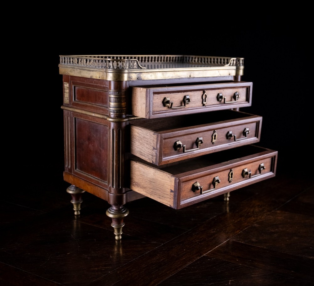 A miniature Louis XVI style mahogany chest of three drawers featuring a white marble top, pierced brass gallery, and metal drawer handles. View V