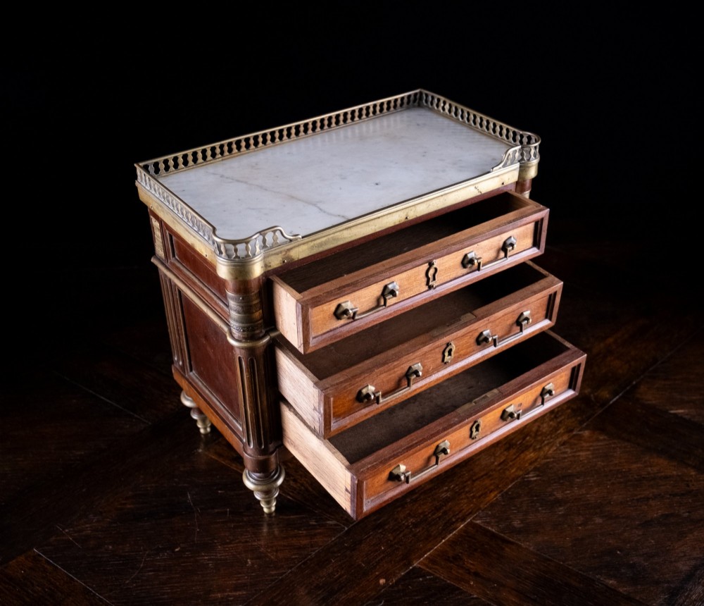 A miniature Louis XVI style mahogany chest of three drawers featuring a white marble top, pierced brass gallery, and metal drawer handles. View VII
