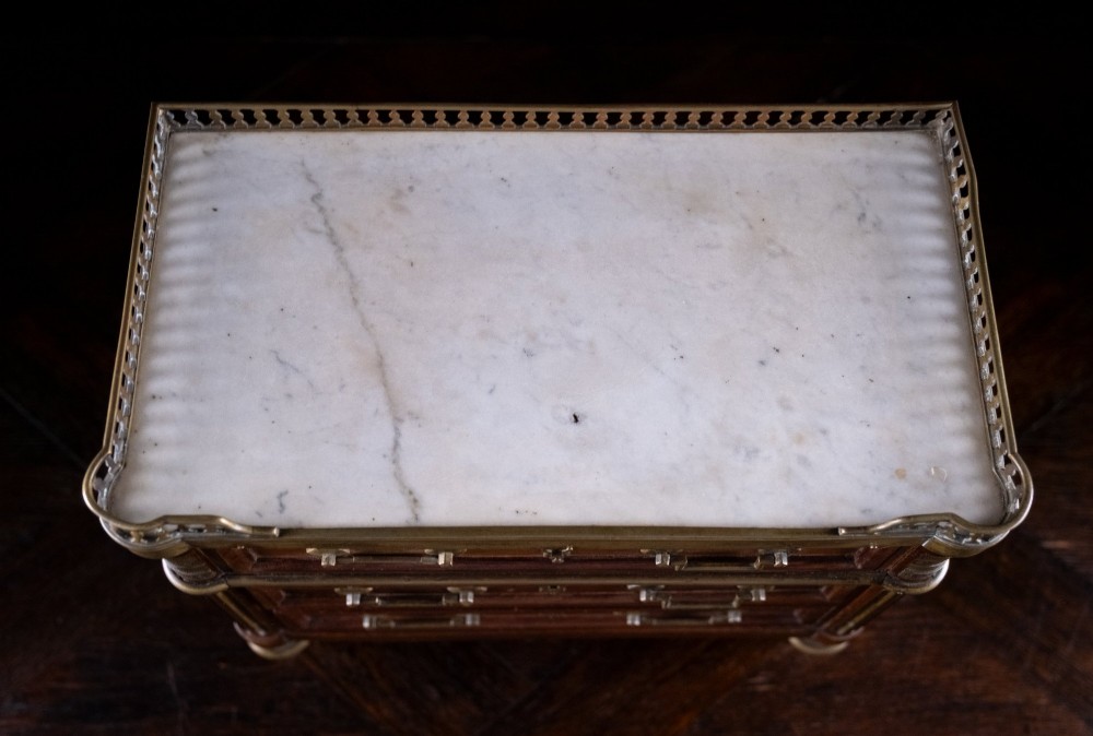 A miniature Louis XVI style mahogany chest of three drawers featuring a white marble top, pierced brass gallery, and metal drawer handles. View VIII