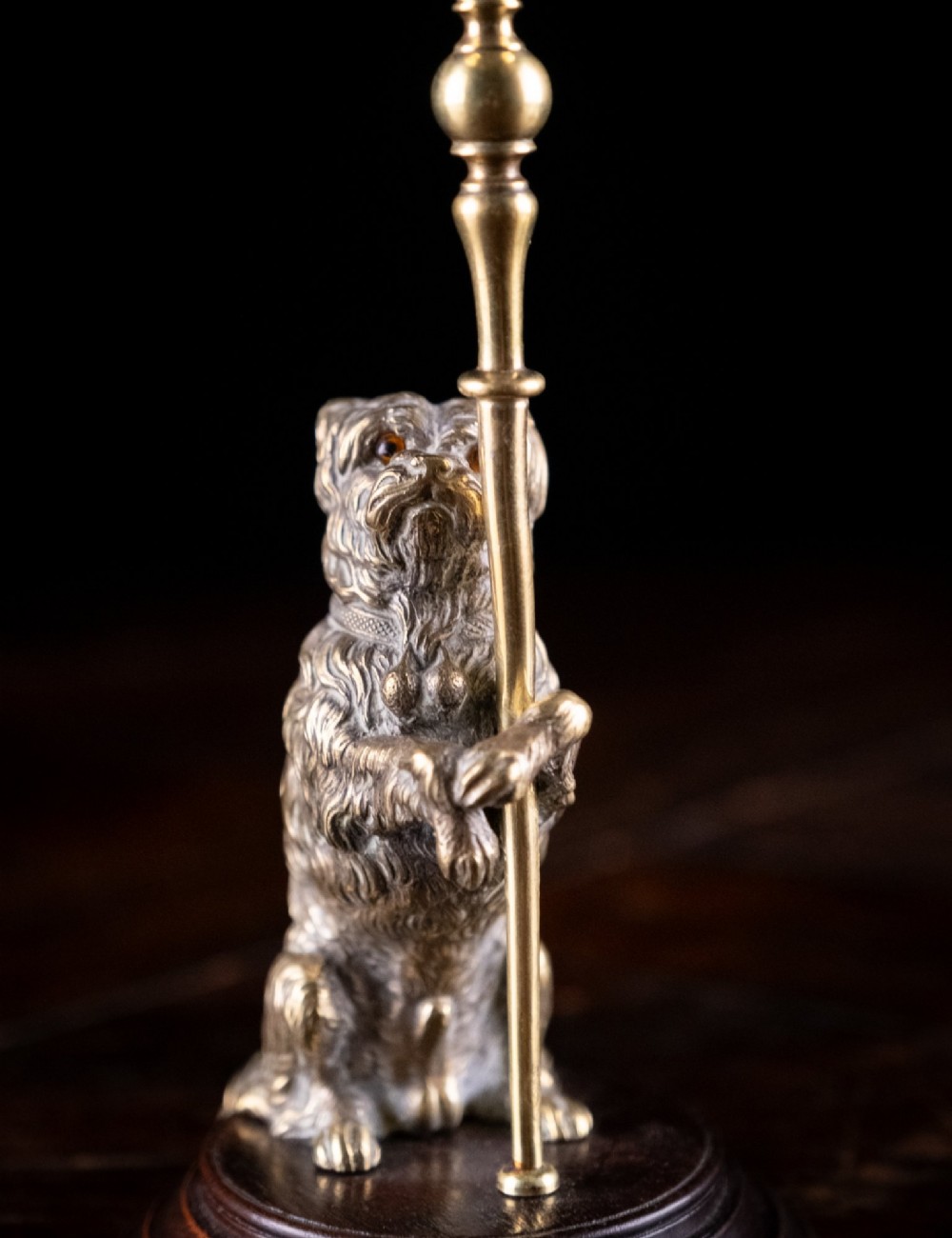 A pair of Edwardian cast brass candlesticks featuring standing terrier dogs holding tall candle columns on dark turned wooden bases. View VI