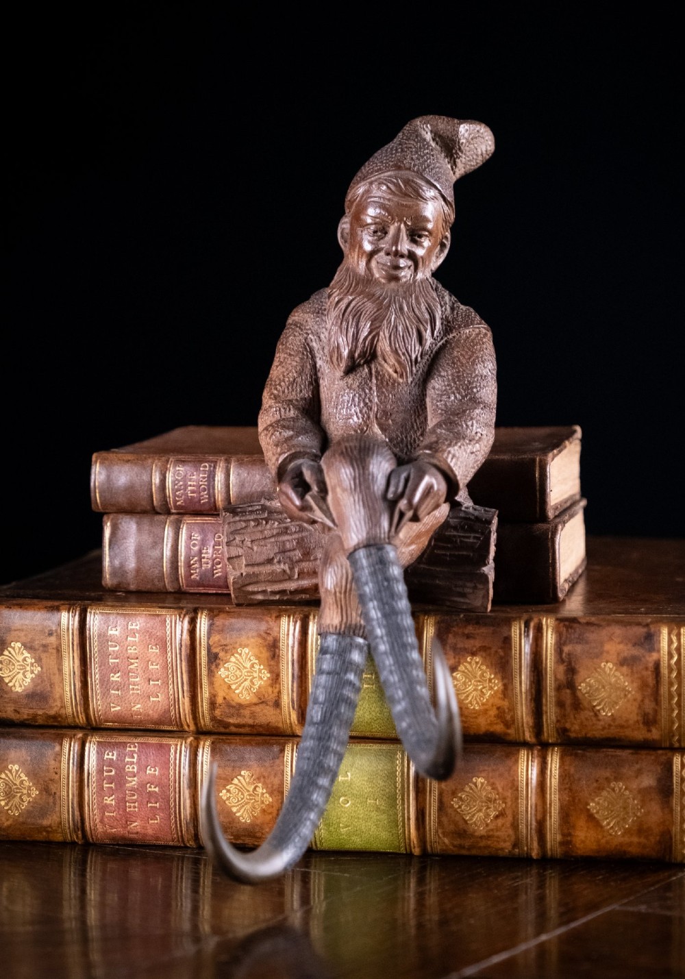 A carved dark wood Black Forest gnome figure seated with curved horn hooks extending below for hanging items. View V