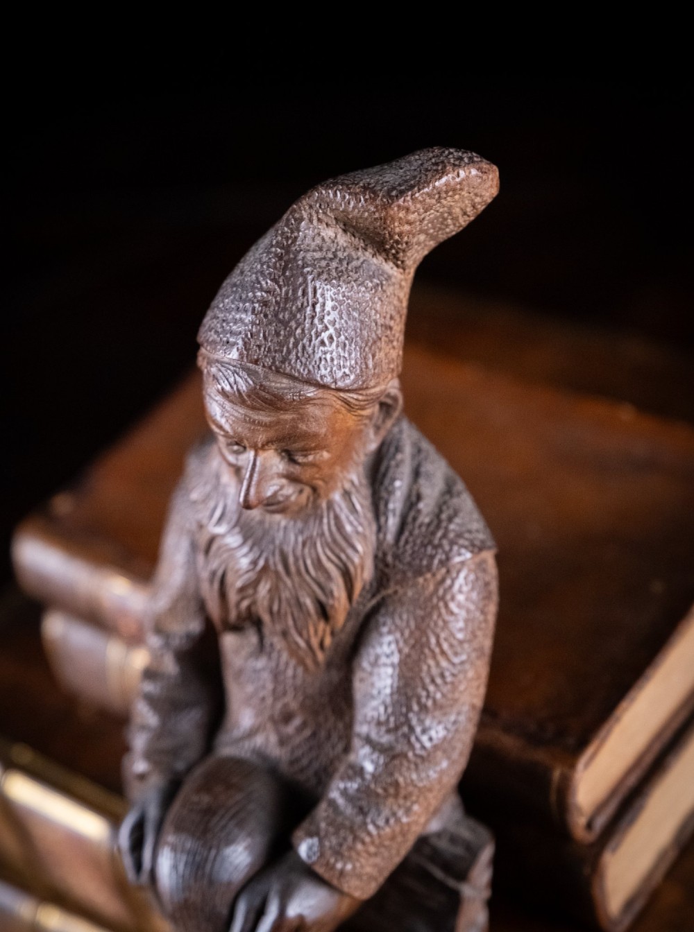 A carved dark wood Black Forest gnome figure seated with curved horn hooks extending below for hanging items. View IX