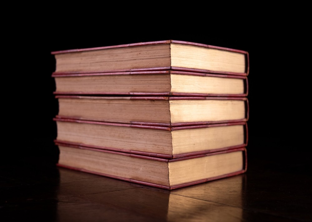 A five-volume set of red books featuring gilt spine lettering and embossed animal motifs. View V
