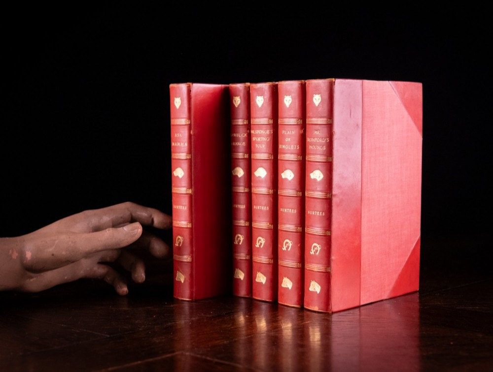 A five-volume set of red books featuring gilt spine lettering and embossed animal motifs. View VI