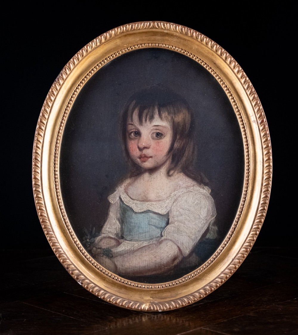 An 18th-century oval oil portrait of a young girl with dark hair in a light blue and white dress, contained within a carved gilt wood frame.