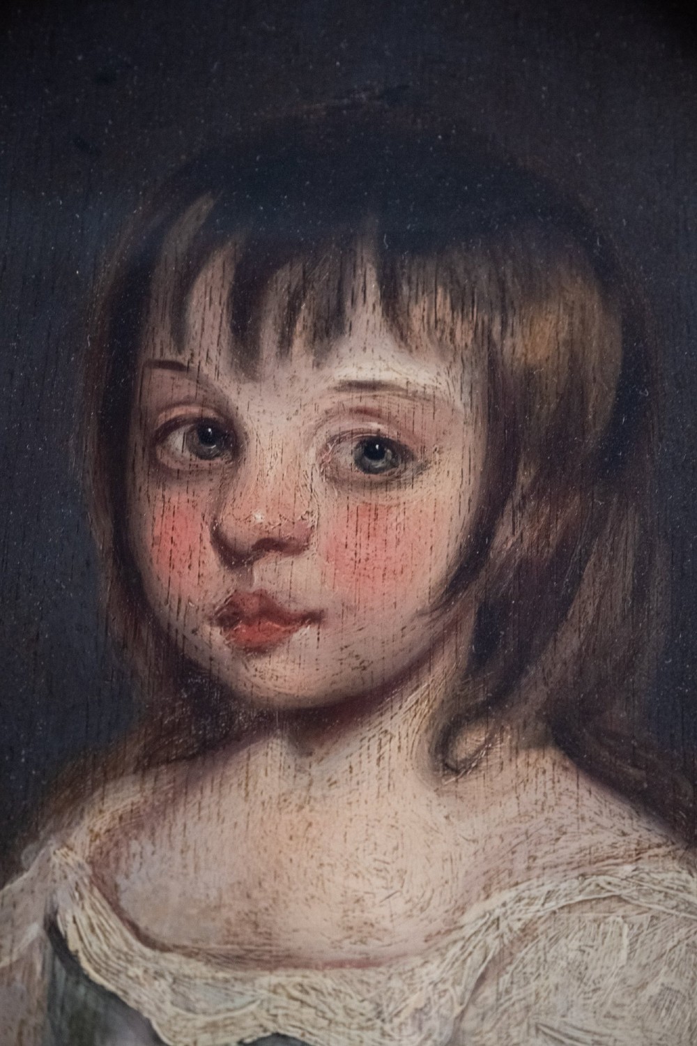 An 18th-century oval oil portrait of a young girl with dark hair in a light blue and white dress, contained within a carved gilt wood frame. View III