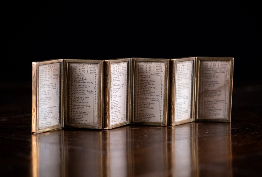 A Victorian six-panel folding brass frame holding a miniature 1878 printed London almanac.