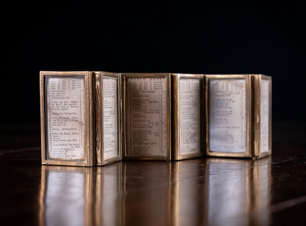 A Victorian six-panel folding brass frame holding a miniature 1878 printed London almanac. View IV