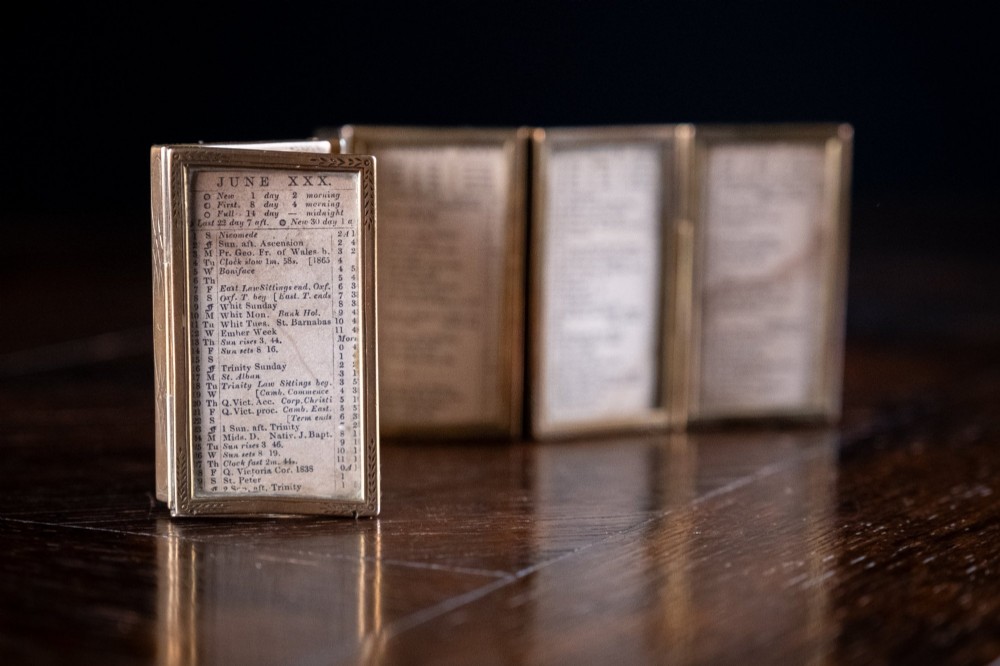 A Victorian six-panel folding brass frame holding a miniature 1878 printed London almanac. View X