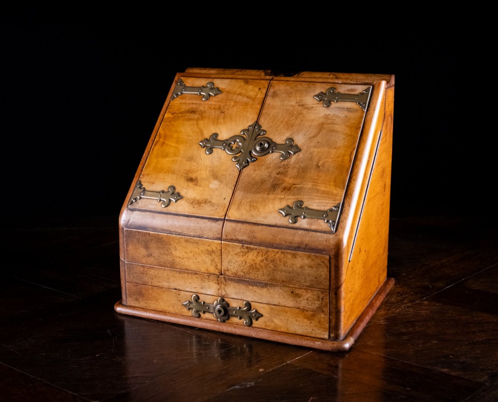 A Victorian walnut stationery cabinet featuring a sloped front with double doors, brass strapwork hinges, and a lower drawer. View V