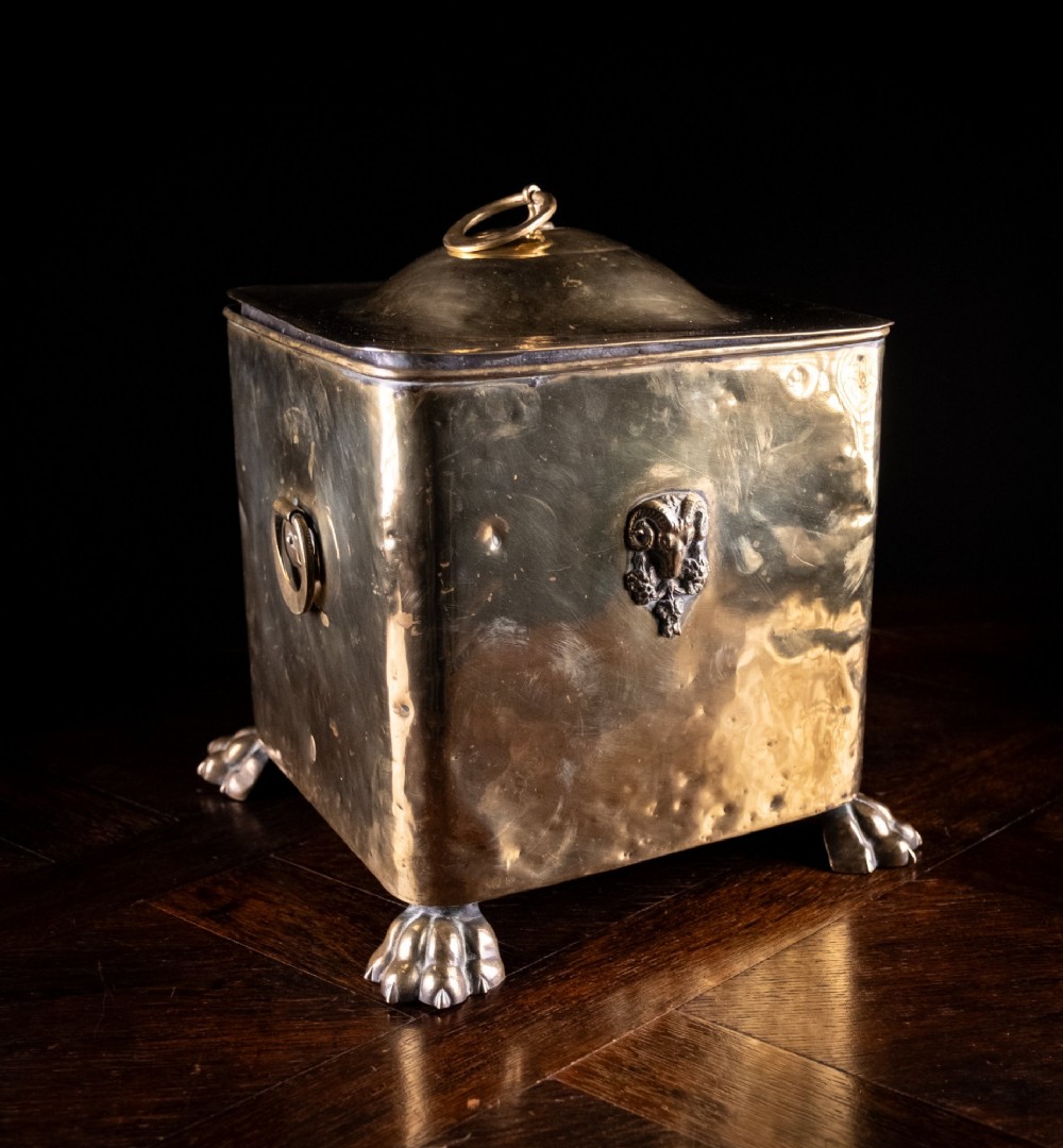 A square Victorian brass coal bin featuring a domed lid with a top ring handle, cast ram head mounts, drop ring handles, and four claw and paw feet.