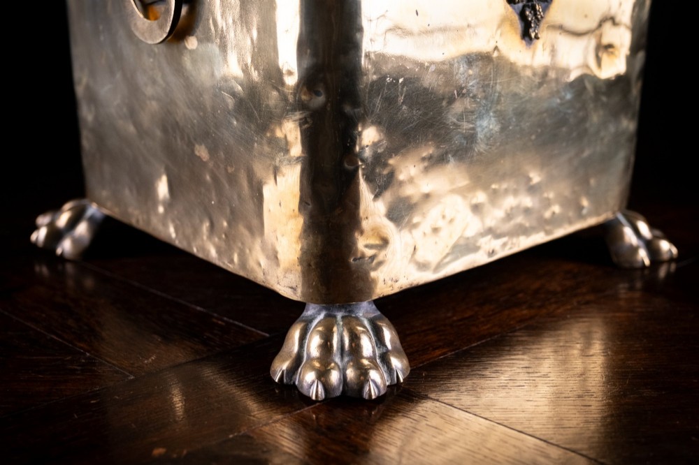 A square Victorian brass coal bin featuring a domed lid with a top ring handle, cast ram head mounts, drop ring handles, and four claw and paw feet. View VI