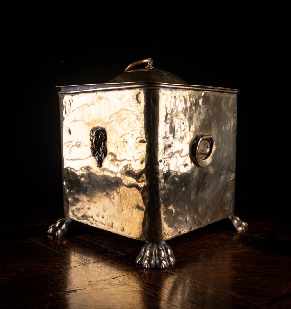 A square Victorian brass coal bin featuring a domed lid with a top ring handle, cast ram head mounts, drop ring handles, and four claw and paw feet. View VII