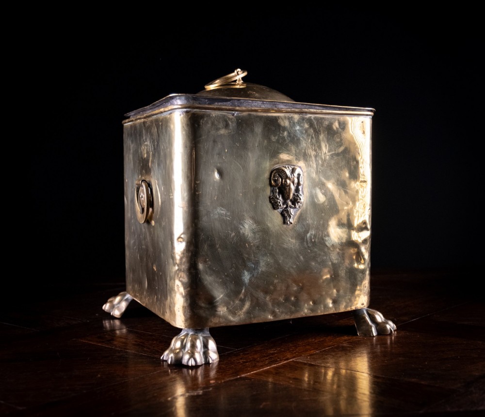 A square Victorian brass coal bin featuring a domed lid with a top ring handle, cast ram head mounts, drop ring handles, and four claw and paw feet. View XII