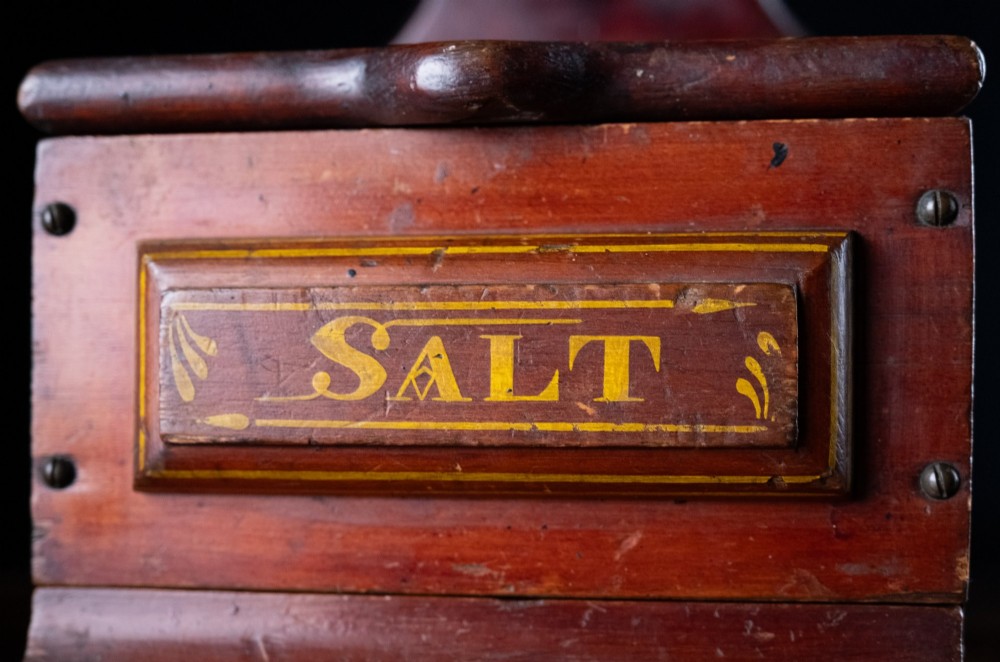 A nineteenth-century reddish-brown painted wooden wall-hanging salt box featuring gilt lettering reading SALT, a sloping hinged lid, and a small bottom drawer. View III