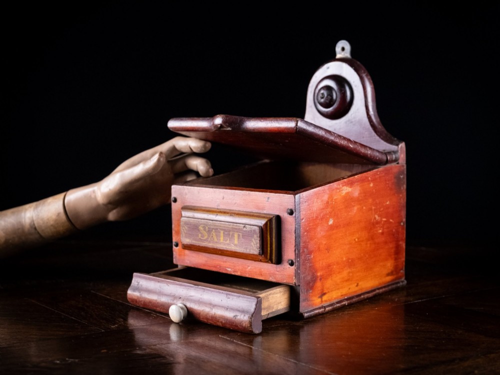 A nineteenth-century reddish-brown painted wooden wall-hanging salt box featuring gilt lettering reading SALT, a sloping hinged lid, and a small bottom drawer. View V