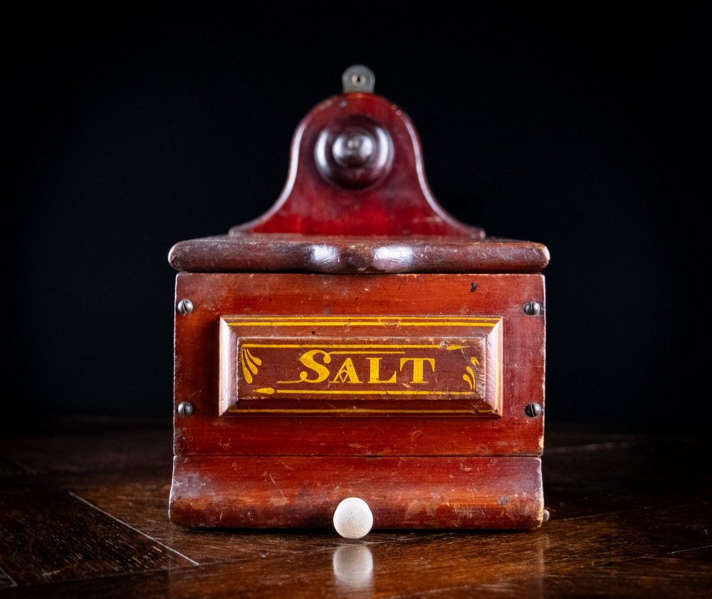A nineteenth-century reddish-brown painted wooden wall-hanging salt box featuring gilt lettering reading SALT, a sloping hinged lid, and a small bottom drawer. View X