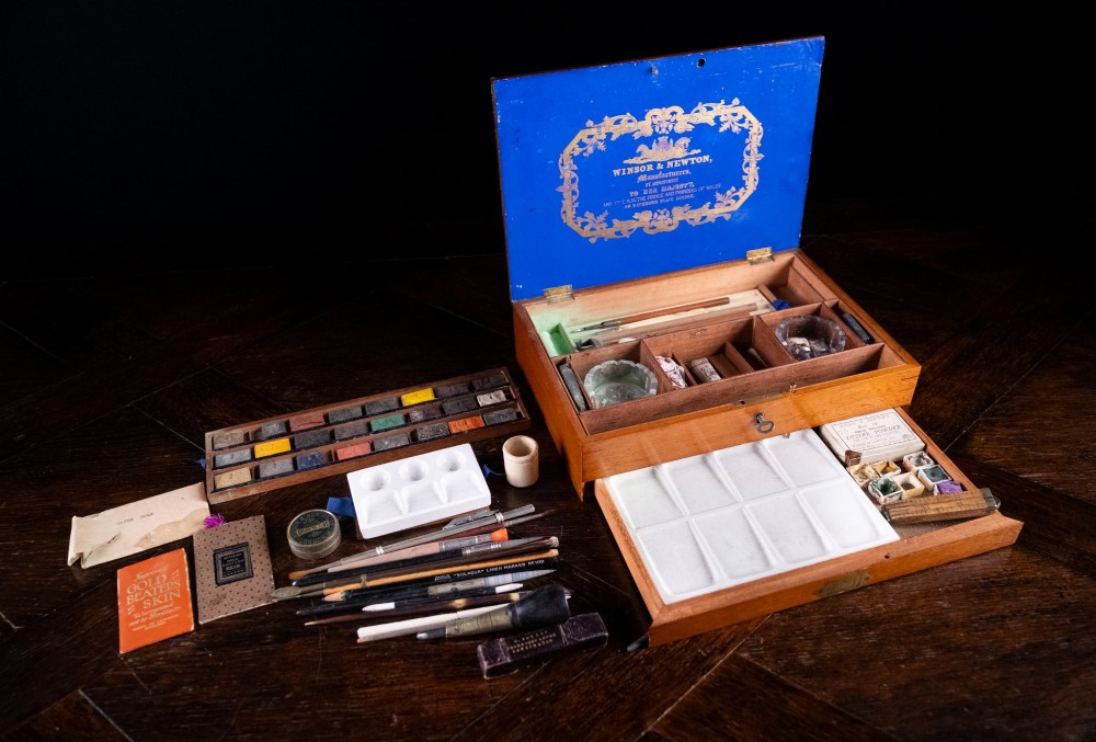 A Victorian mahogany artist watercolour box featuring an open lid lined with blue gilt-stamped paper, fitted compartments containing colour cakes, glass dishes, and a lower drawer holding a ceramic palette. View II
