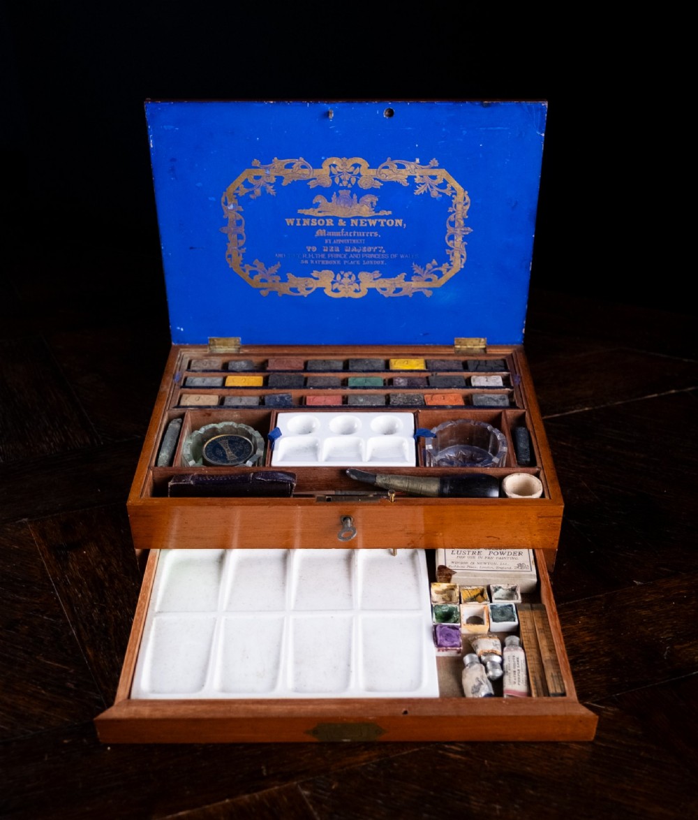 A Victorian mahogany artist watercolour box featuring an open lid lined with blue gilt-stamped paper, fitted compartments containing colour cakes, glass dishes, and a lower drawer holding a ceramic palette. View IV