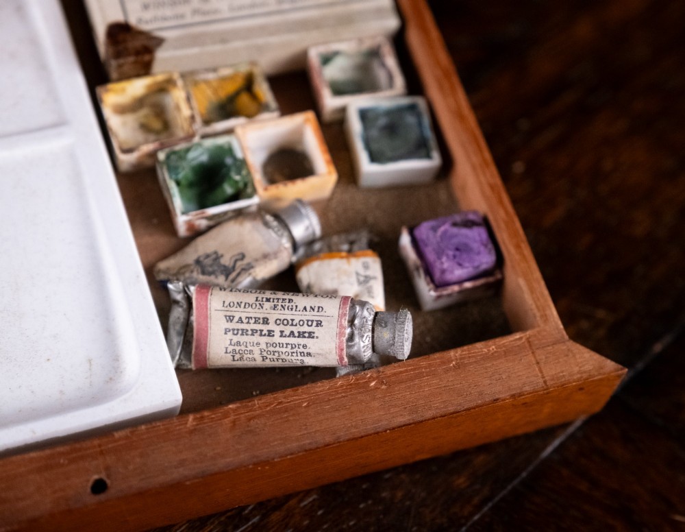 A Victorian mahogany artist watercolour box featuring an open lid lined with blue gilt-stamped paper, fitted compartments containing colour cakes, glass dishes, and a lower drawer holding a ceramic palette. View X
