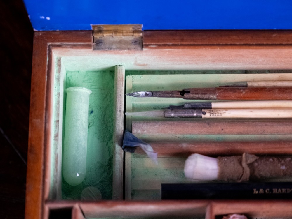 A Victorian mahogany artist watercolour box featuring an open lid lined with blue gilt-stamped paper, fitted compartments containing colour cakes, glass dishes, and a lower drawer holding a ceramic palette. View XIII