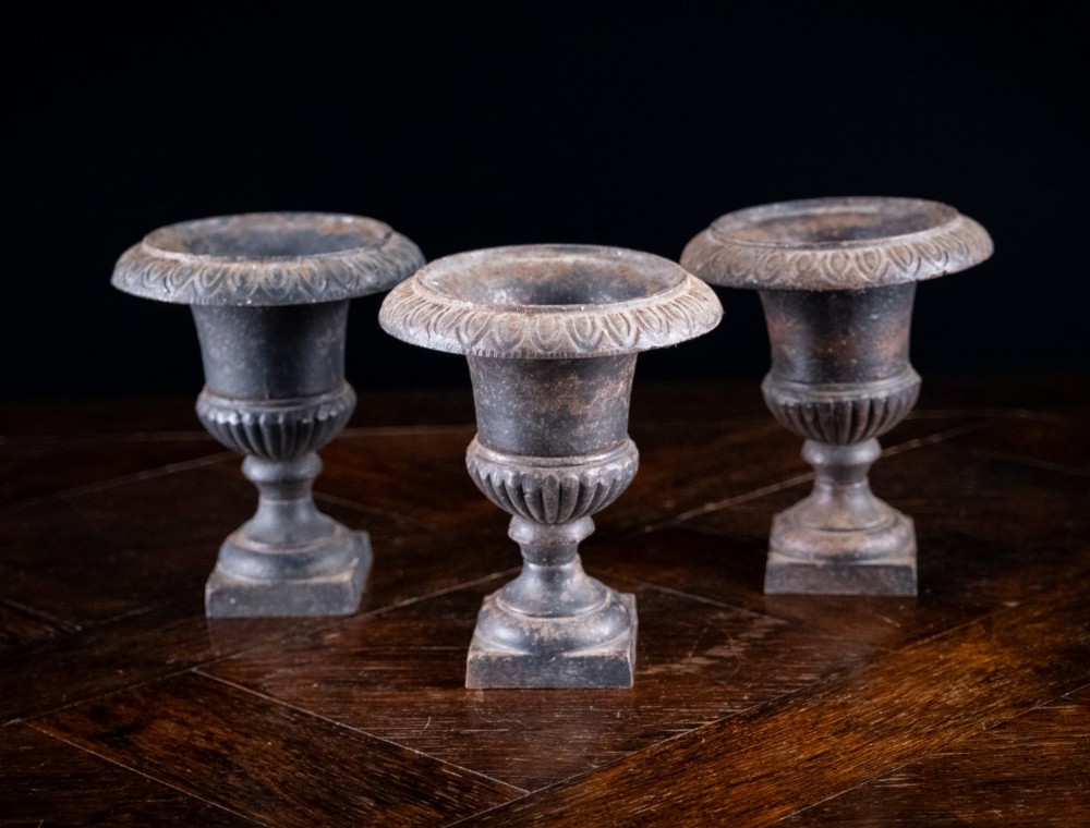 A set of three miniature cast iron urns featuring fluted campana bodies and square pedestal bases with a dark patinated finish. View IV