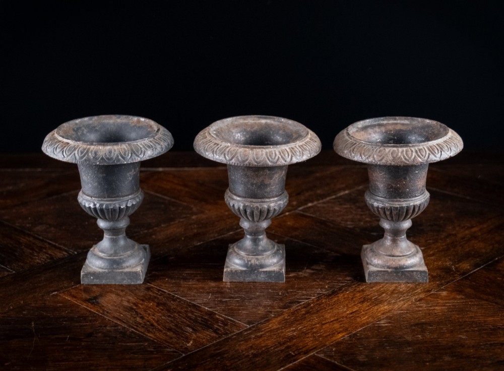 A set of three miniature cast iron urns featuring fluted campana bodies and square pedestal bases with a dark patinated finish. View V