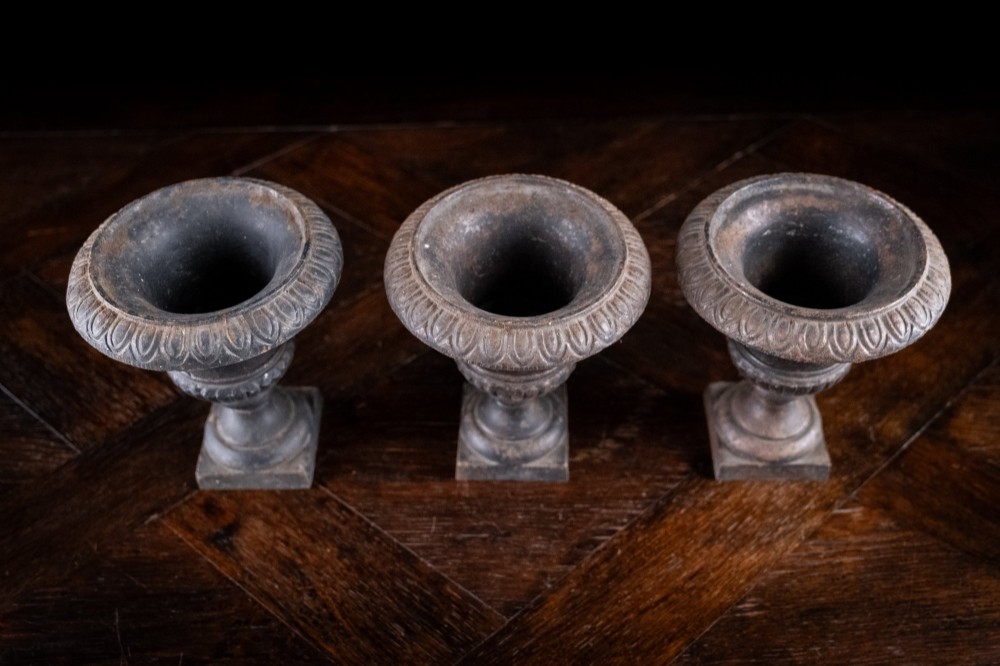 A set of three miniature cast iron urns featuring fluted campana bodies and square pedestal bases with a dark patinated finish. View VI