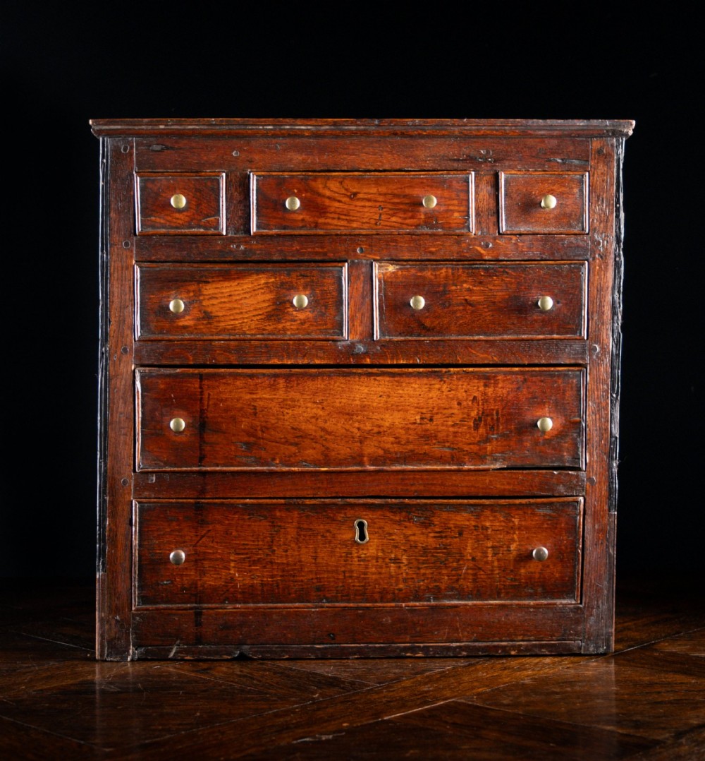 An 18th-century dark oak tabletop chest of drawers featuring seven multi-sized drawers with brass knob handles and a brass keyhole escutcheon. View II