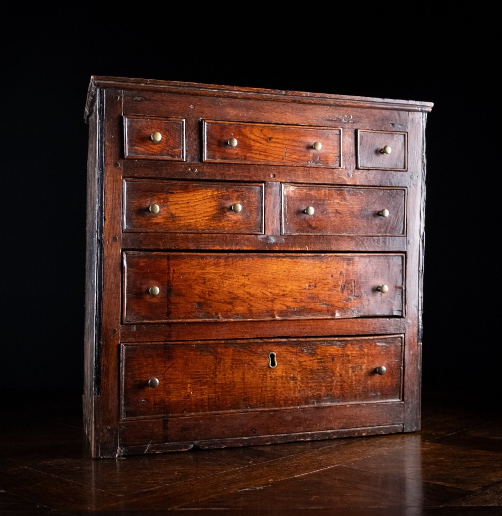 An 18th-century dark oak tabletop chest of drawers featuring seven multi-sized drawers with brass knob handles and a brass keyhole escutcheon. View III