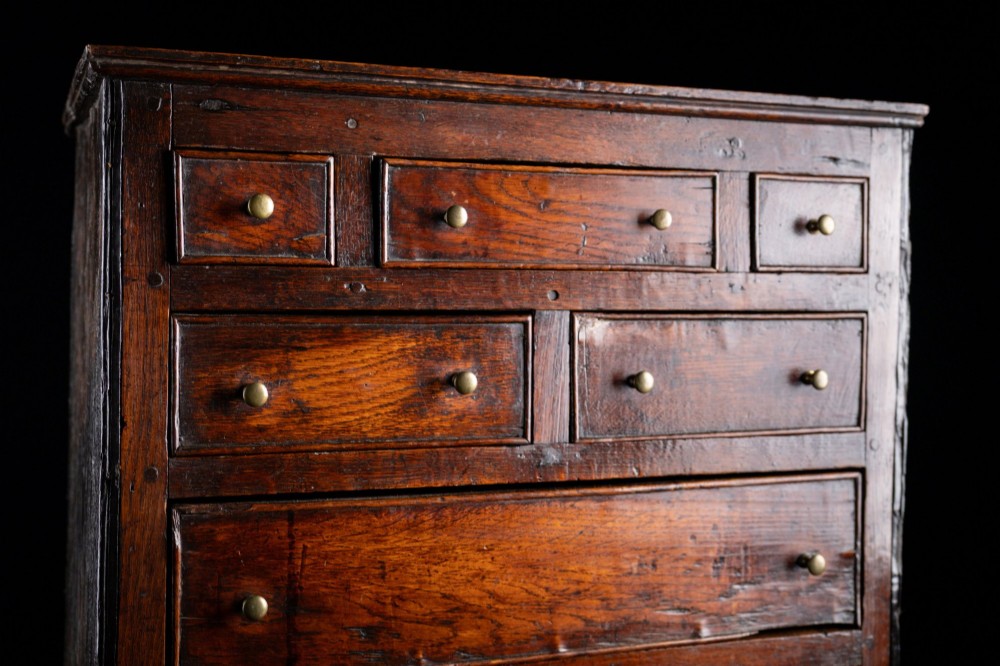 An 18th-century dark oak tabletop chest of drawers featuring seven multi-sized drawers with brass knob handles and a brass keyhole escutcheon. View IV