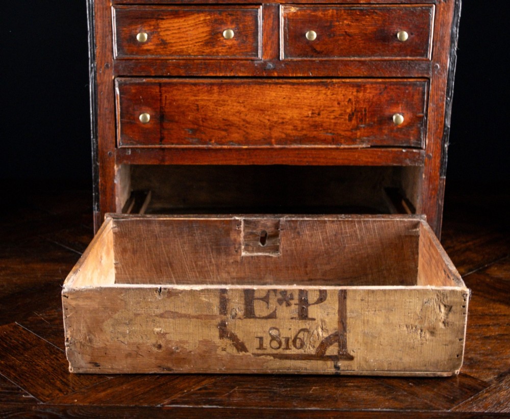 An 18th-century dark oak tabletop chest of drawers featuring seven multi-sized drawers with brass knob handles and a brass keyhole escutcheon. View VIII