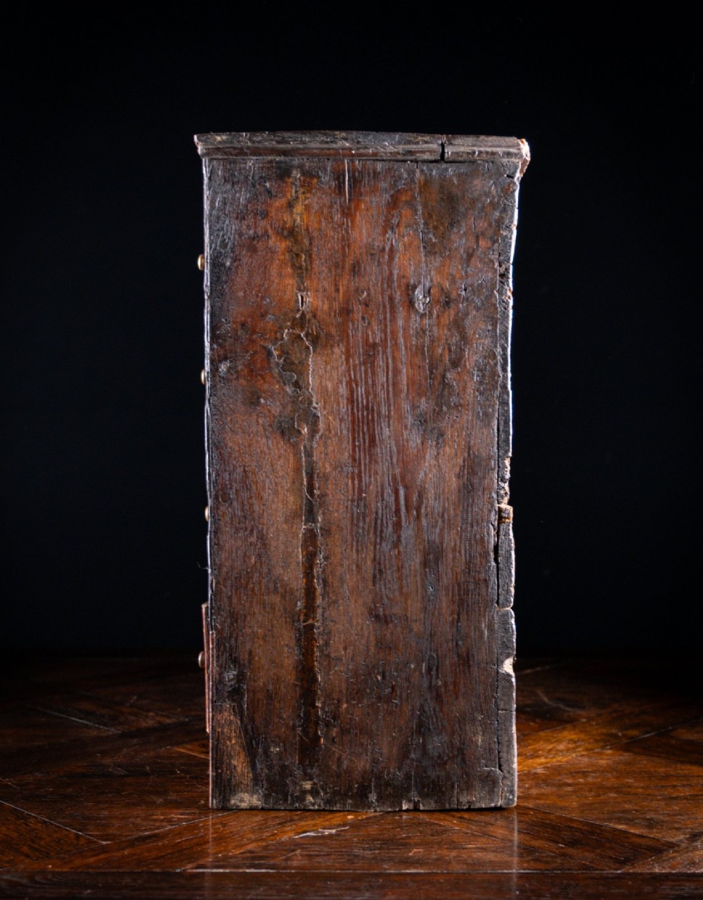 An 18th-century dark oak tabletop chest of drawers featuring seven multi-sized drawers with brass knob handles and a brass keyhole escutcheon. View XII