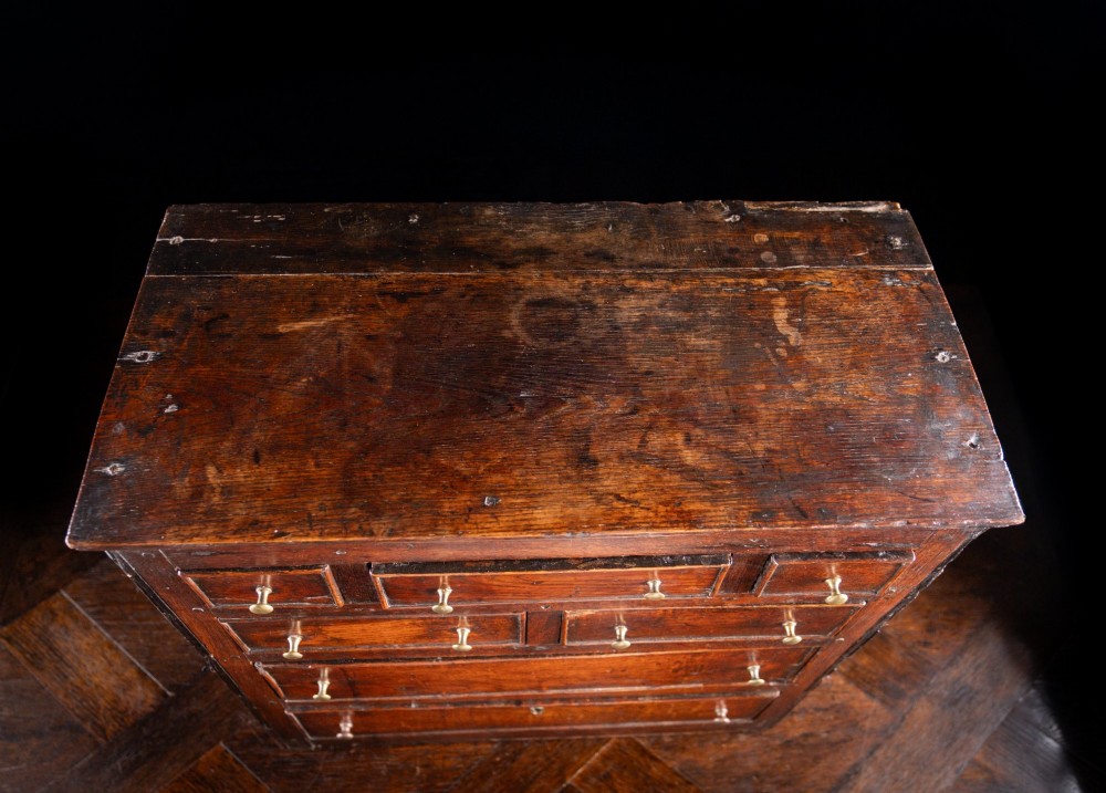 An 18th-century dark oak tabletop chest of drawers featuring seven multi-sized drawers with brass knob handles and a brass keyhole escutcheon. View XIII