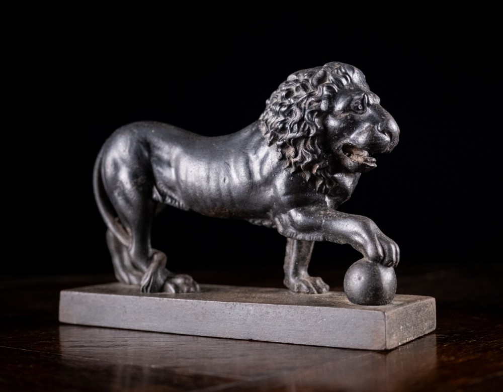 A dark cast iron lion sculpture standing on a rectangular base with one front paw resting on a sphere.
