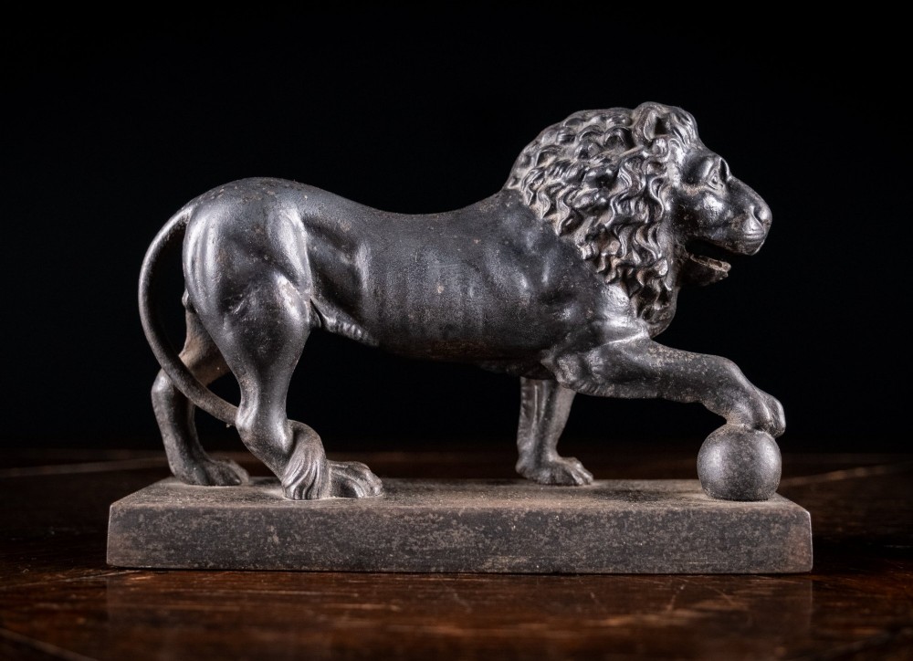 A dark cast iron lion sculpture standing on a rectangular base with one front paw resting on a sphere. View II