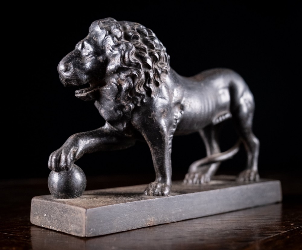 A dark cast iron lion sculpture standing on a rectangular base with one front paw resting on a sphere. View V