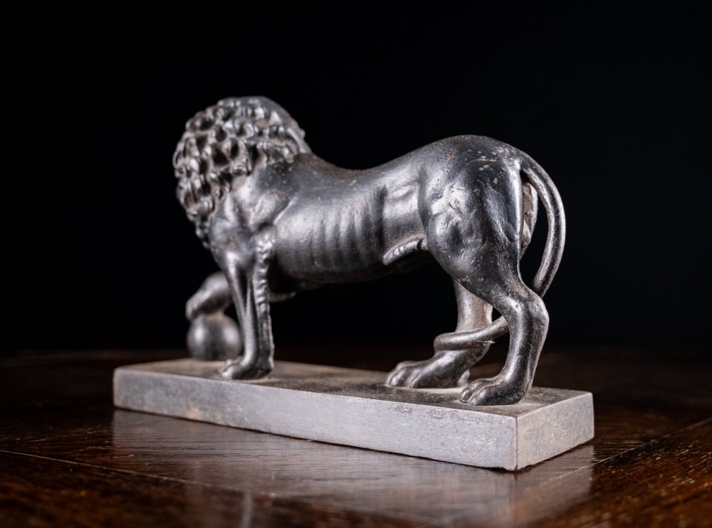 A dark cast iron lion sculpture standing on a rectangular base with one front paw resting on a sphere. View VII
