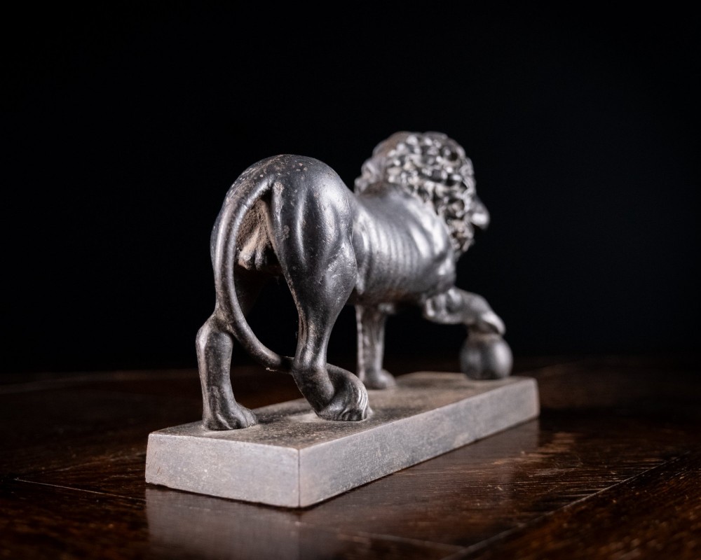 A dark cast iron lion sculpture standing on a rectangular base with one front paw resting on a sphere. View VIII