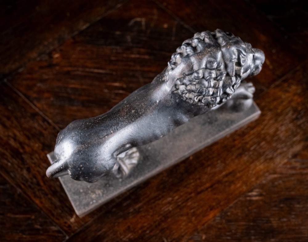 A dark cast iron lion sculpture standing on a rectangular base with one front paw resting on a sphere. View IX
