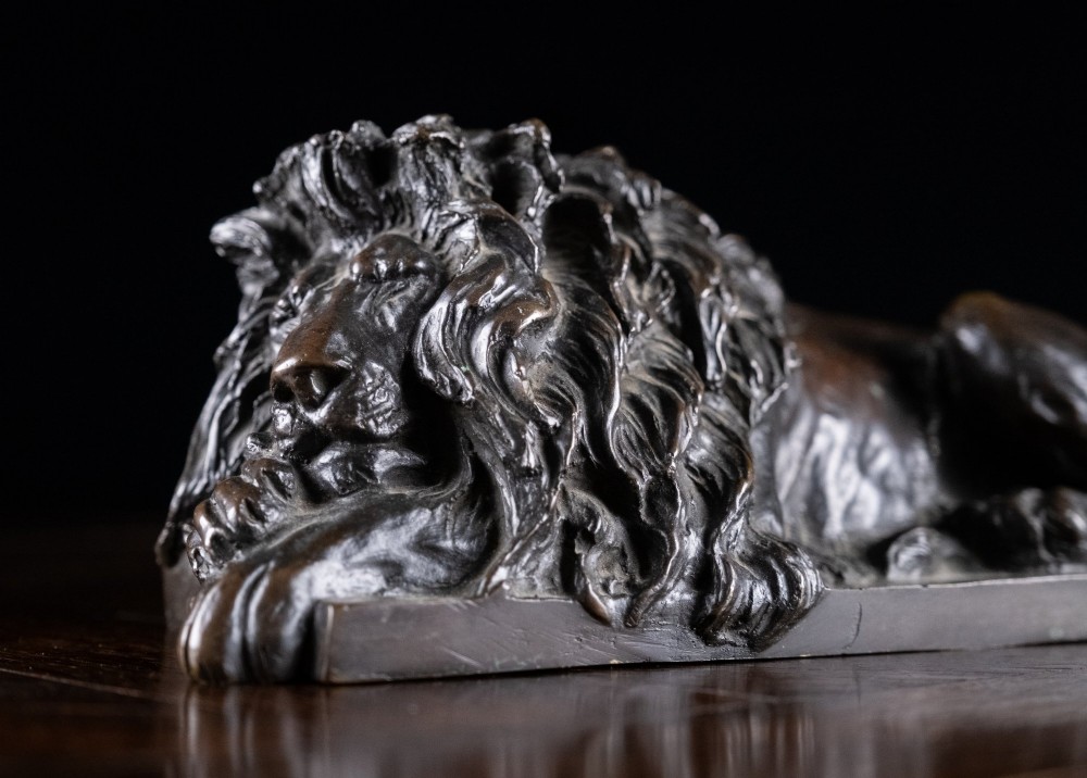 A dark brown patinated bronze sculpture depicting a recumbent sleeping lion resting its head on an integrated rectangular base. View II