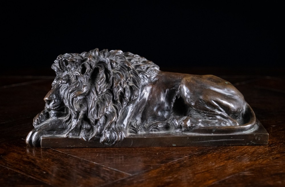 A dark brown patinated bronze sculpture depicting a recumbent sleeping lion resting its head on an integrated rectangular base. View III