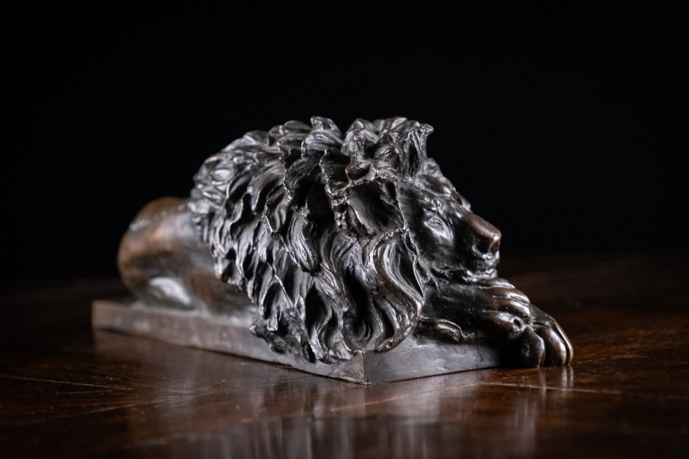 A dark brown patinated bronze sculpture depicting a recumbent sleeping lion resting its head on an integrated rectangular base. View IV
